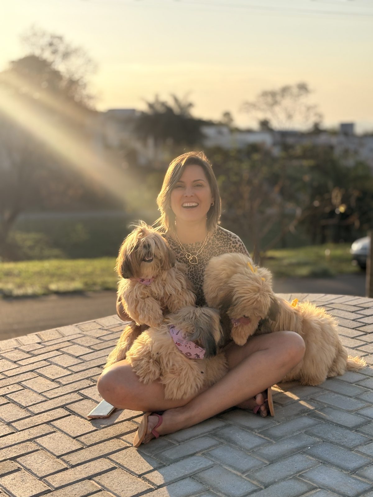 Cliente sorrindo ao ar livre com seus dois poodles no colo